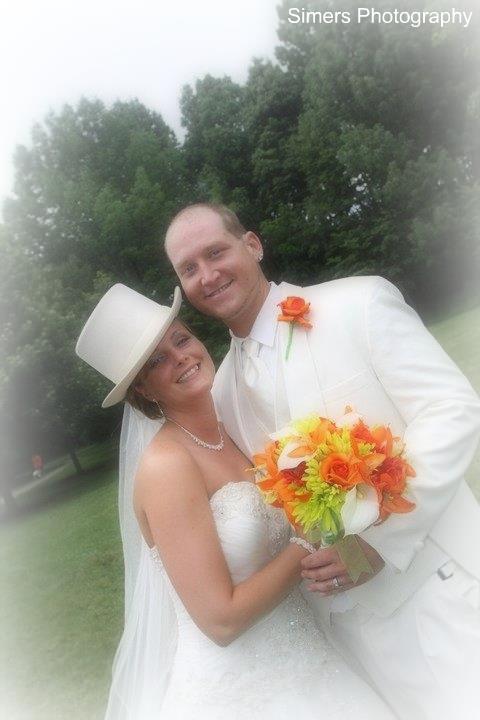 Wedding couple embracing with vibrant orange and yellow artificial flower bouquet, showcasing Forever Flowers by Val's custom design